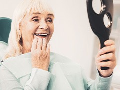 An older woman admiring her dentures with a hand mirror