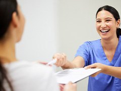 Dental assistant smiling while handing patient form