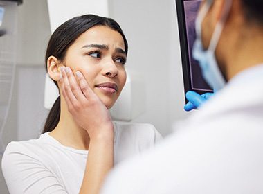 A woman frowning and touching her cheek while talking to her dentist